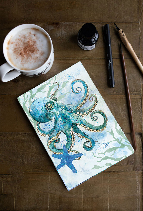 notebook with watercolour octopus and starfish motif by dollyhotdogs, with assorted pens and a mug of coffee